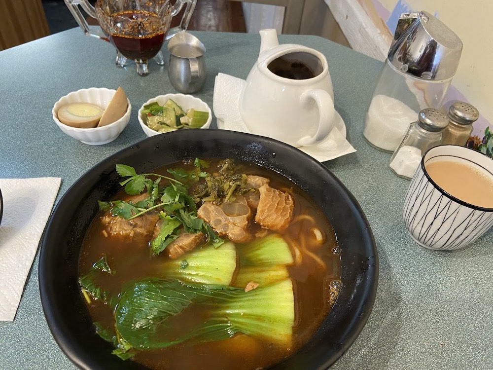 Beef tendon noodle soup with bok choy and cilantro, served with a braised egg and a cucumber side dish
